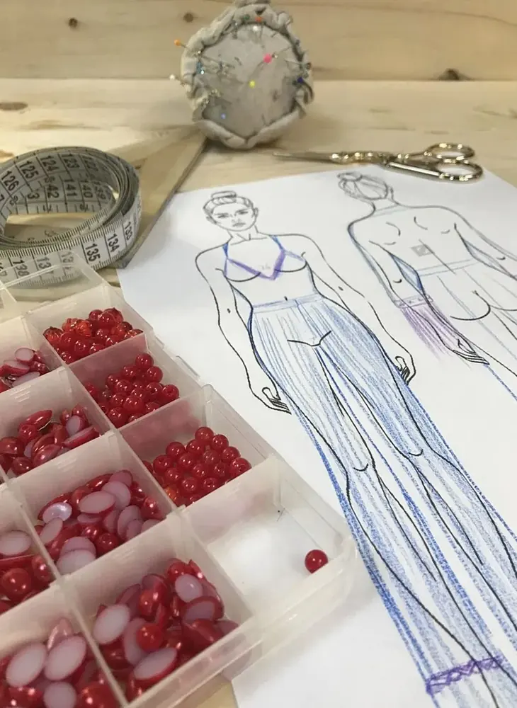 ファッションのデザイン画、ビーズ、メジャーが並んだ作業台